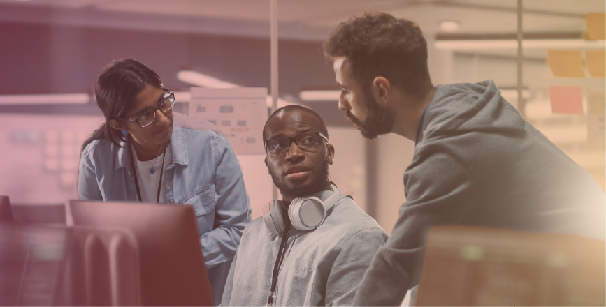 A group of three individuals in casual attire collaborate at a desk, with one wearing headphones and looking thoughtfully at the others.