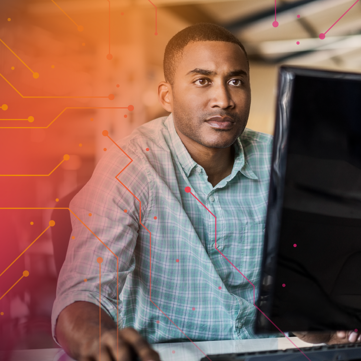 A focused man sitting at a computer, working intently with a blurred digital interface overlay in warm colours.