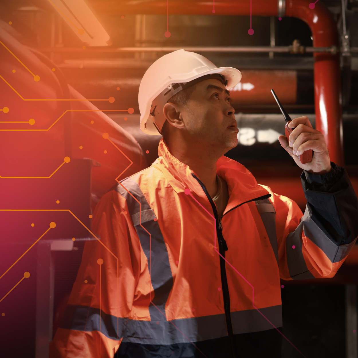 A worker in a hard hat and safety jacket stands in an industrial setting, holding a smartphone and looking upwards thoughtfully.