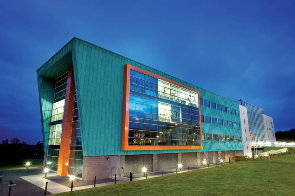 Modern architectural building with a striking turquoise and orange façade, illuminated against a twilight sky.