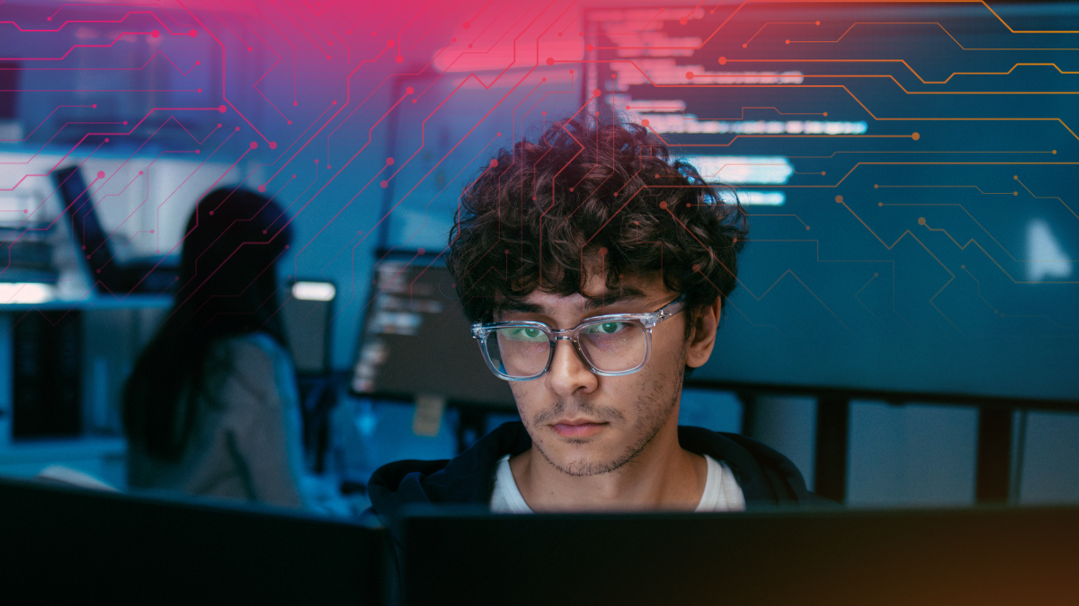 A young man with curly hair and glasses focuses intently on computer screens, surrounded by a digital-themed background.