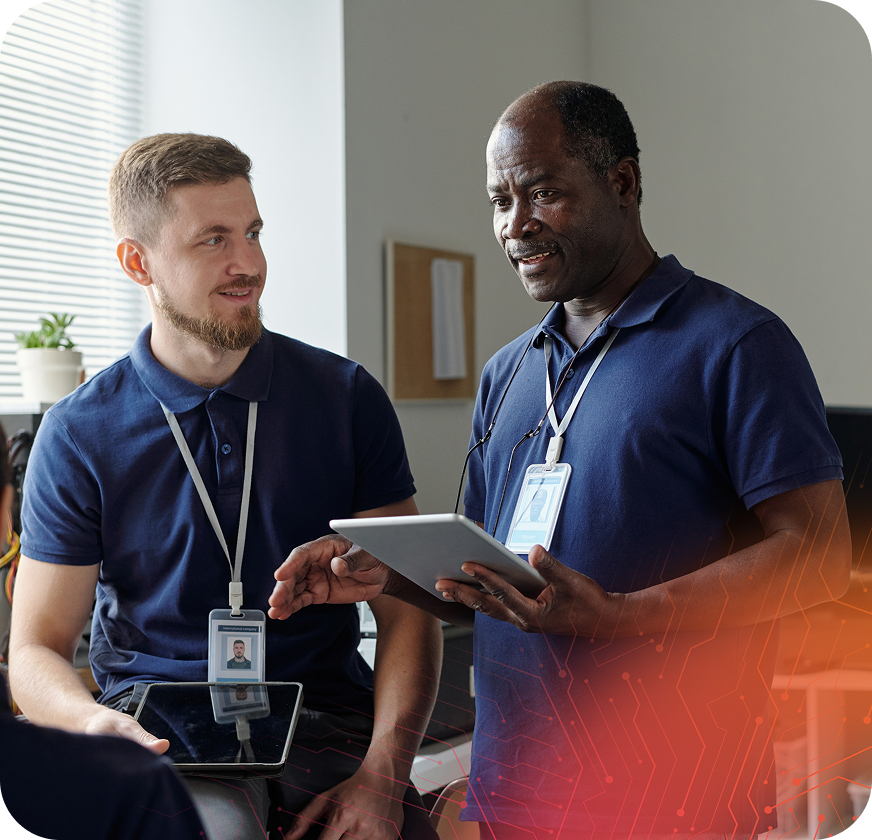 Two men in blue polo shirts engage in conversation while one holds a tablet. They are in a well-lit office with plants and a modern ambiance.