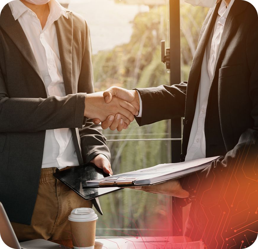 Two business professionals shake hands, exchanging documents in a well-lit office setting, with greenery visible outside.