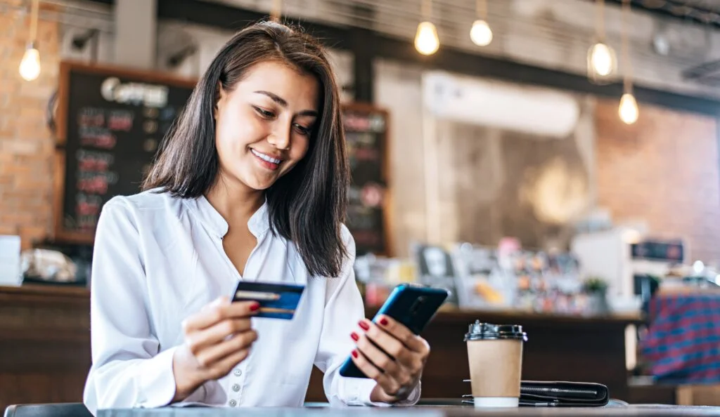 Young woman pay for goods by credit card through a smartphone in a coffee shop