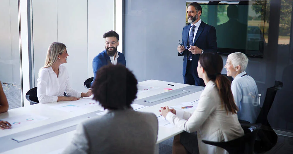 Business man and female assistant addressing meeting in meeting room smiling at colleagues